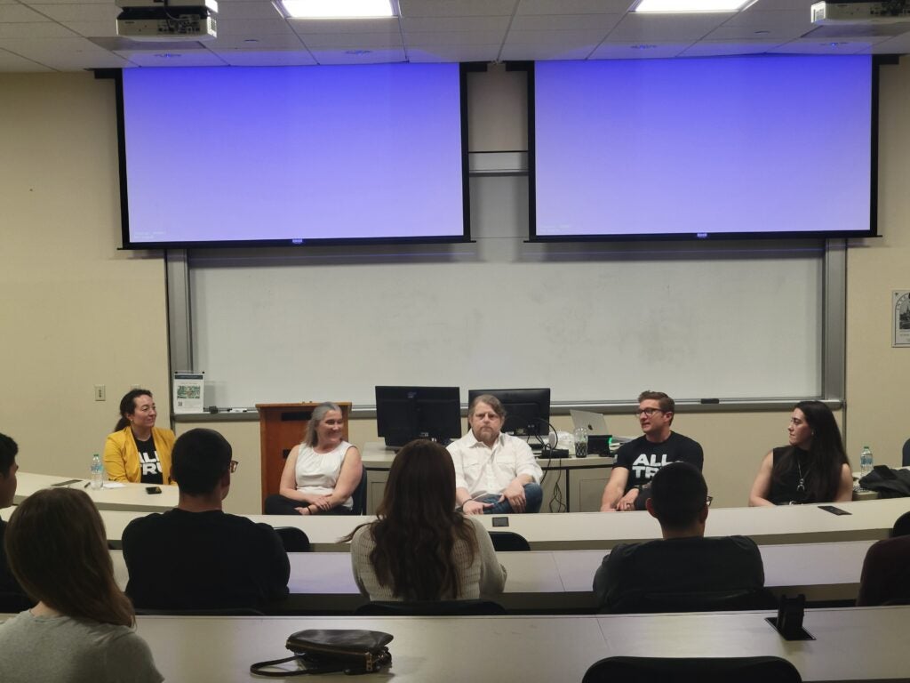 5 presenters sitting in a row speaking to seated students