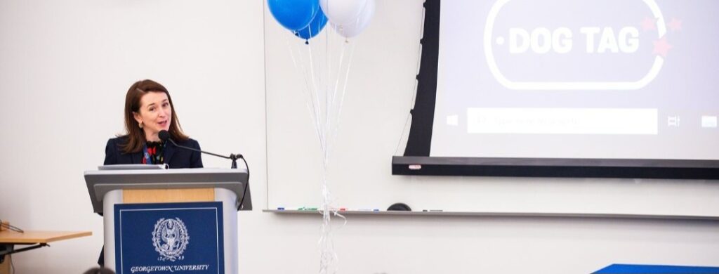 Speaker at Georgetown university podium with dog tag bakery logo on board behind her