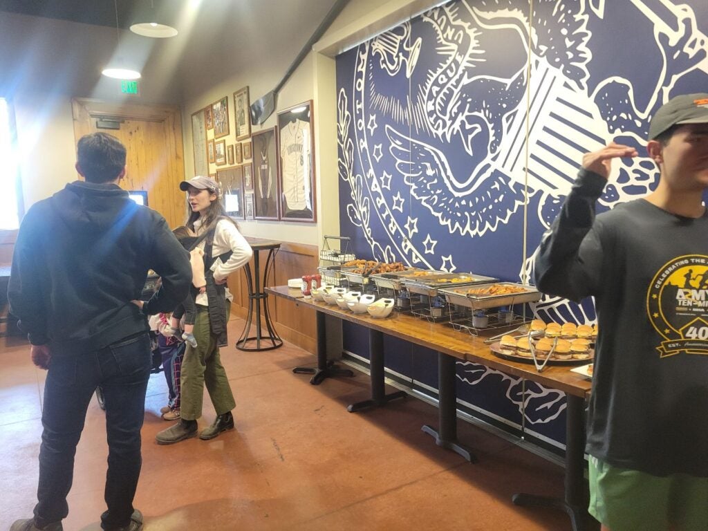 A casual gathering in a room with blue and white wall art, featuring an eagle. A buffet table holds various dishes. Three people chat casually.