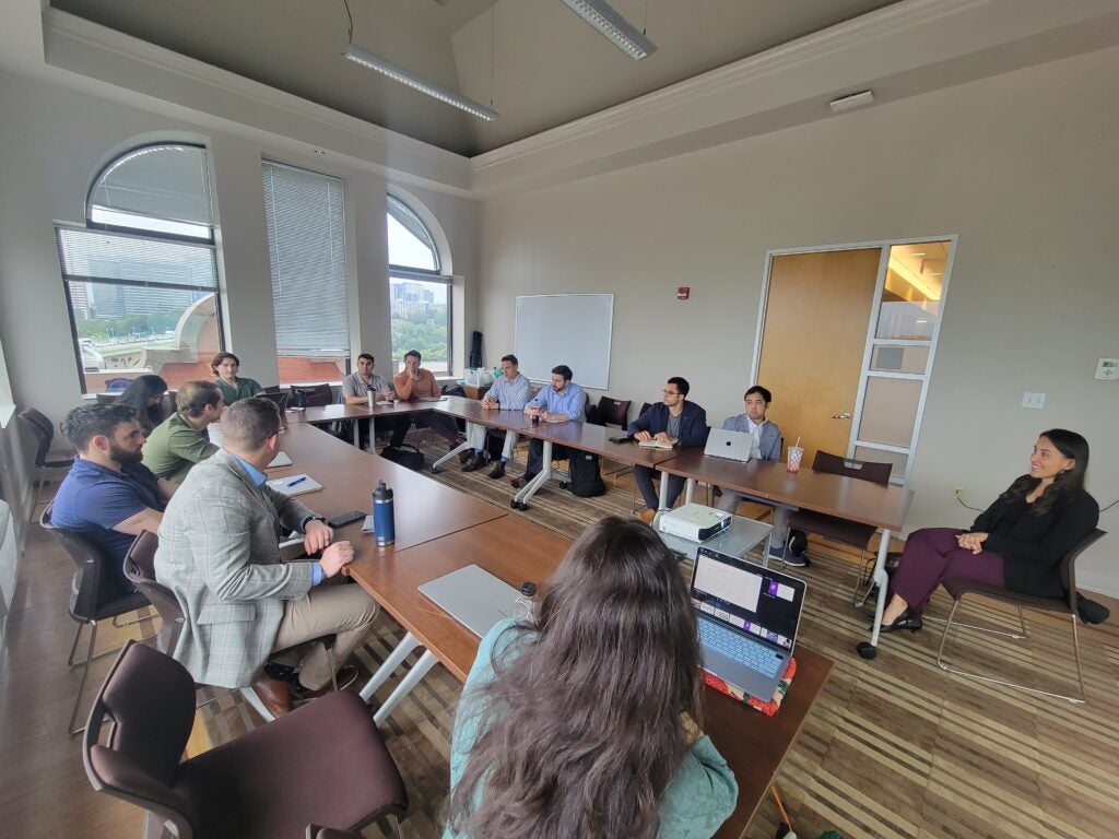 People sitting around a u-shaped table listening to a speaker