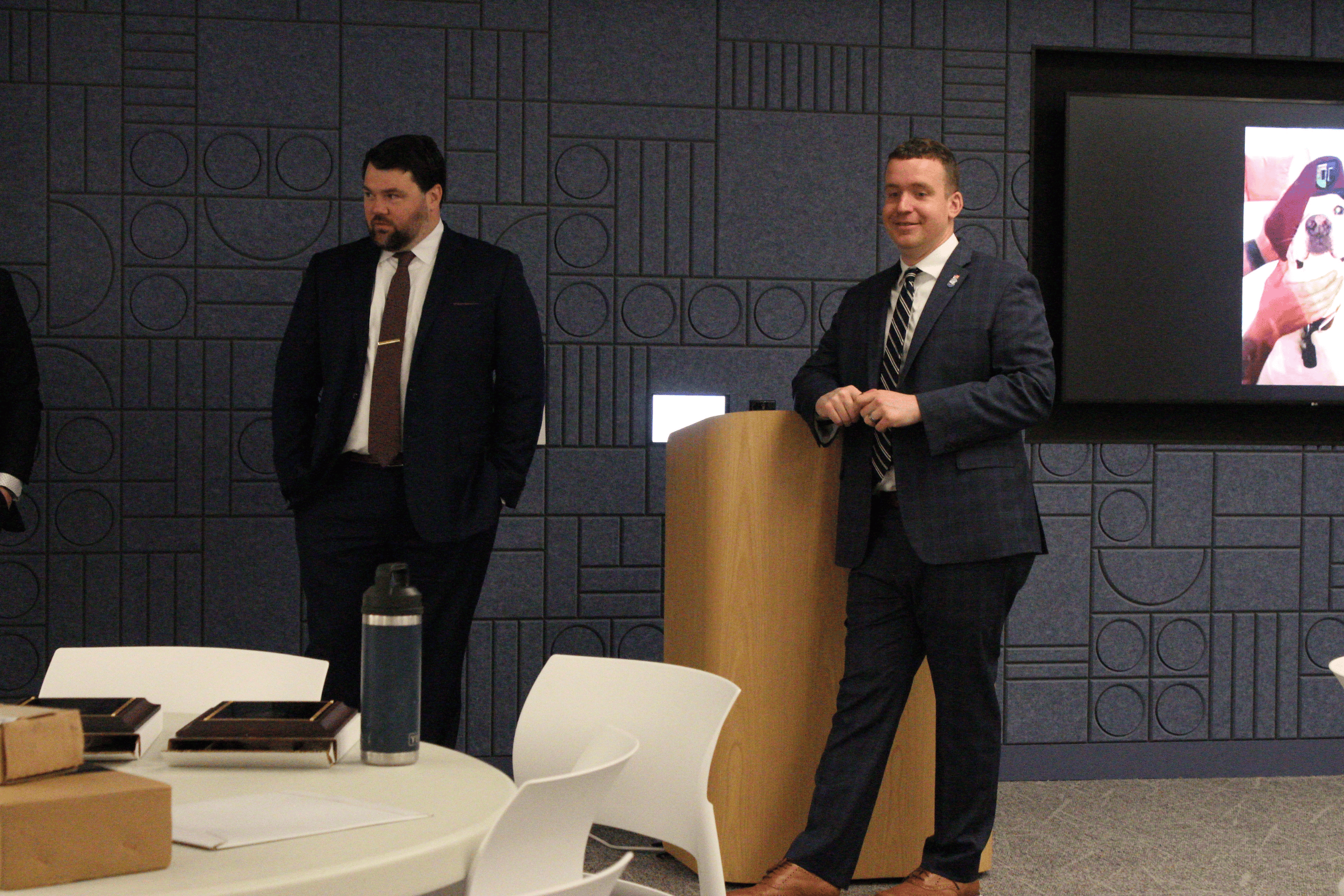 Two men standing near a podium speaking to people