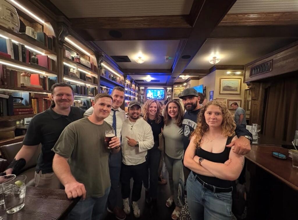 A group of people posing for a photo in a bar, some holding drinks