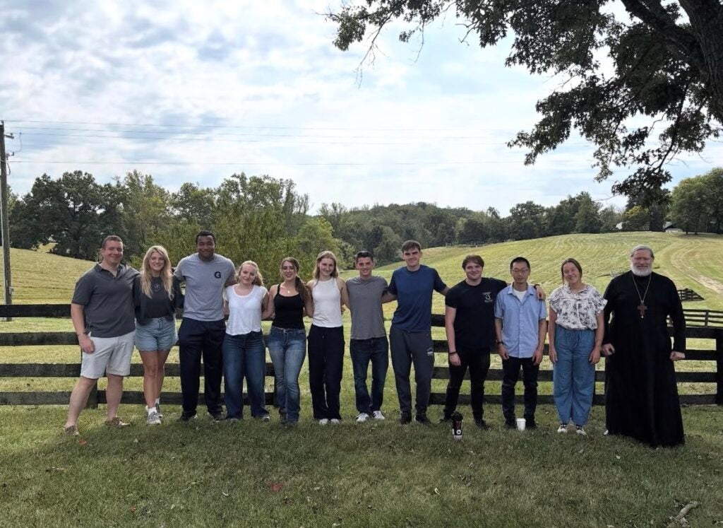 A row of people standing in a line for a picture in front of a fence in a field