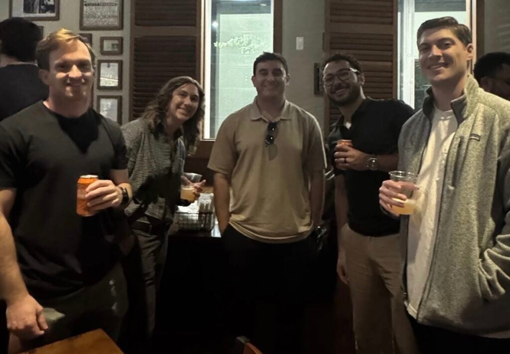 A group of 5 people holding drinks posing for a photo