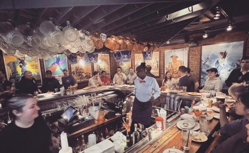 A group of people sitting around a u-shaped bar with a bartender standing in the middle
