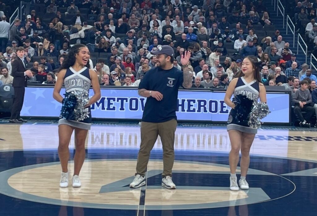 A man waving next to two cheerleaders on a basketball court