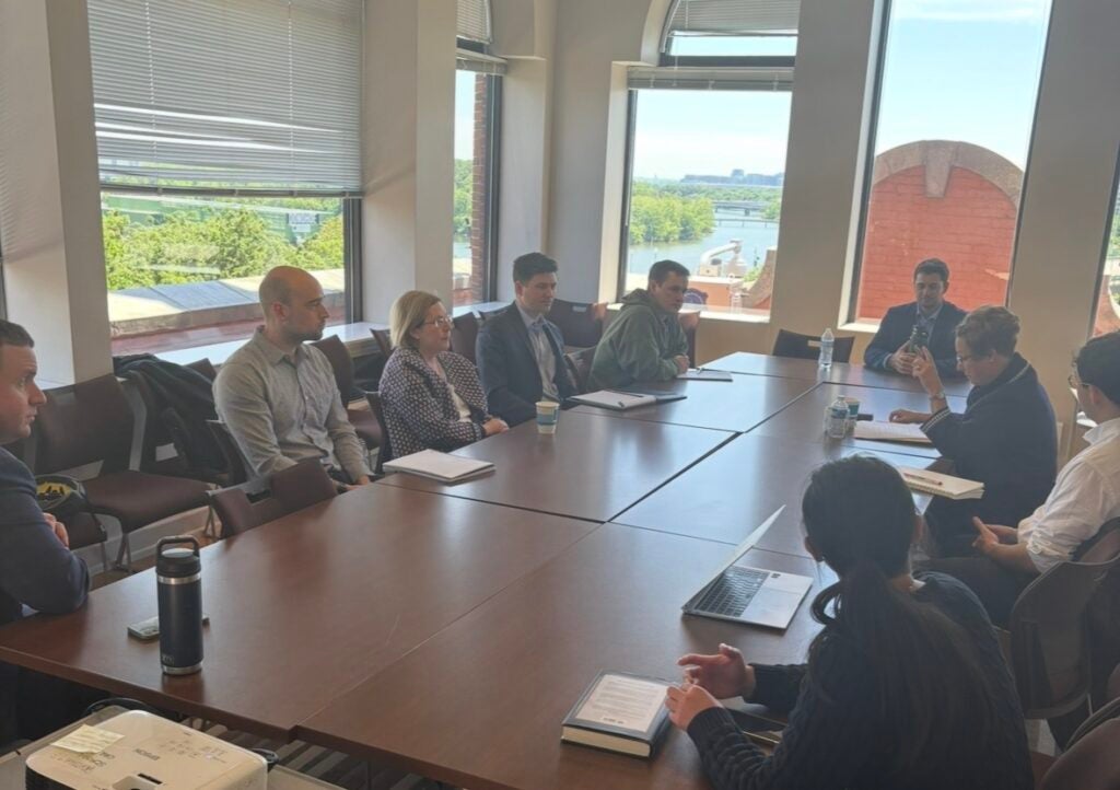 A group of people sitting around a table listening to a speaker also seated
