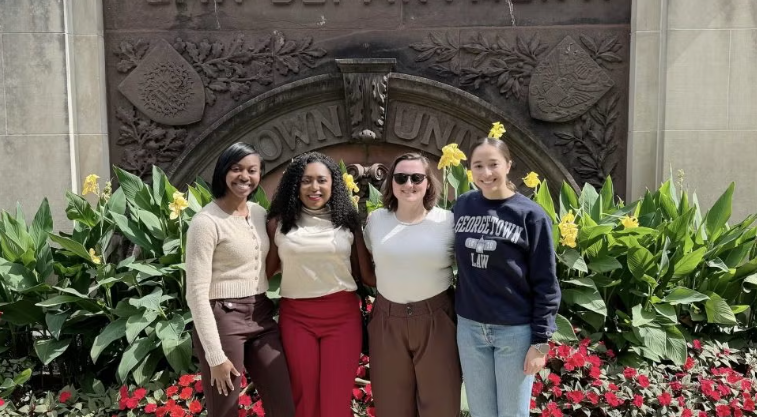 Four women stand in front of a garden with a Georgetown arch in the back