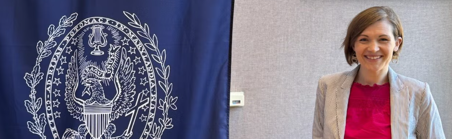 A woman smiles and poses for a picture next to a flag with a Georgetown seal